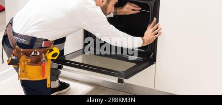 Professional serviceman repairing modern oven in kitchen Stock Photo