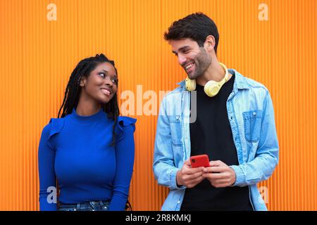 Multi-ethnic couple looking at each other while using headphones and mobile phone. Technology and relationship concept. Stock Photo