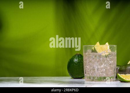 Cold iced Ti punch alcohol cocktail, small punch, rum-based mixed drink with fresh lime slice garnish, on high-colored green background Stock Photo