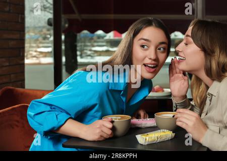Young women with coffee and eclairs spending time together in cafe Stock Photo