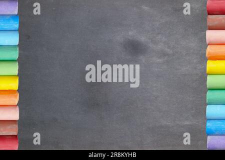 Two rows of colored chalks facing each other on a blank blackboard. Stock Photo
