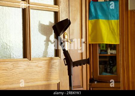 An elbow crutch stands near the door in the apartment and on the background of the flag of Ukraine, rehabilitation after an injury in the war in Ukrai Stock Photo