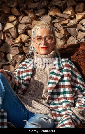 Portrait of fashionable senior woman with cool haircut relaxing next to firewood pile Stock Photo