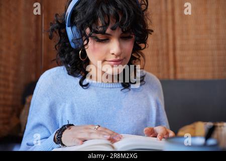 Young woman in headphones reading book while studying Stock Photo