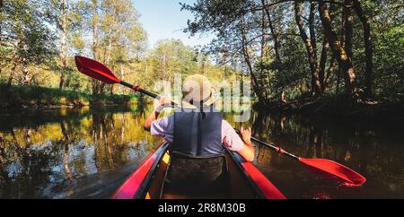 Back Rear View strong caucasian woman rowing Kayaking In Beautiful Lithuania countryside river - Zemeina. Action Camera POV Of Girl Paddling On canoe. Stock Photo