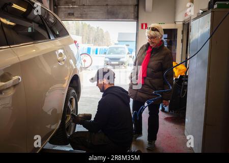 Mechanic in garage changing tires on car and talking to female client Stock Photo