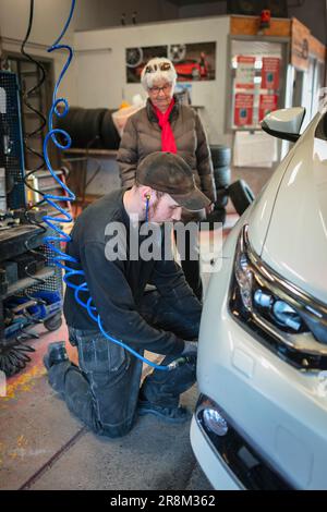 Mechanic in garage changing tires on car and talking to female client Stock Photo
