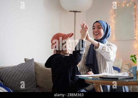Mother wearing hijab helping son doing homework and doing high five Stock Photo
