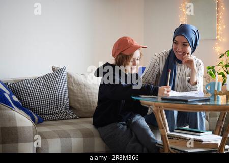 Mother wearing hijab helping son doing homework Stock Photo