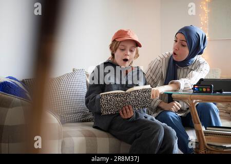 Mother wearing hijab helping son doing homework Stock Photo