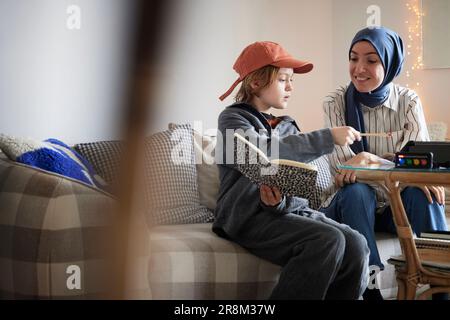 Mother wearing hijab helping son doing homework Stock Photo