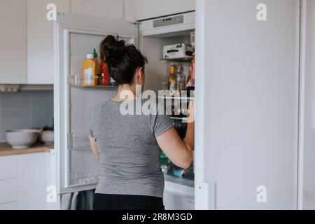 Rear view of woman standing in front of open fridge Stock Photo