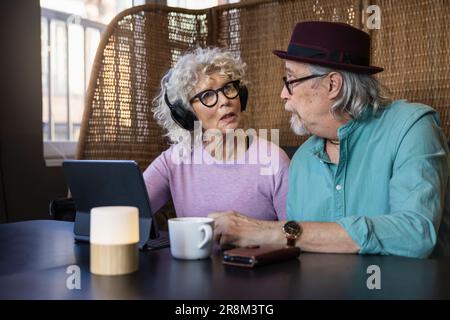 Senior couple sitting in cafe talking while working on digital tablet Stock Photo