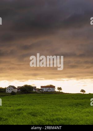 Dramatic storm clouds over meadow with houses in the horizon Stock Photo