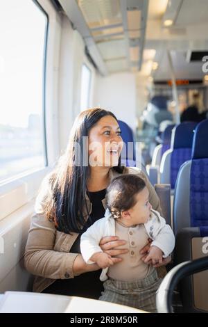 Smiling woman sitting in train with baby on her laps Stock Photo