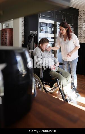 Mother giving disabled teenage daughter in wheelchair drink Stock Photo