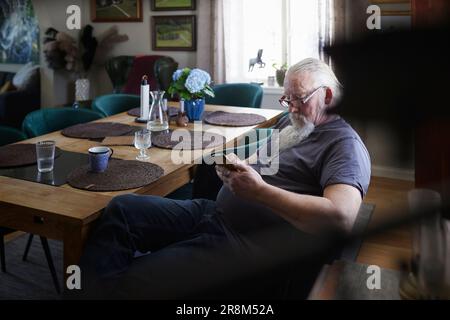 Mature man sitting at dining table and using cell phone Stock Photo