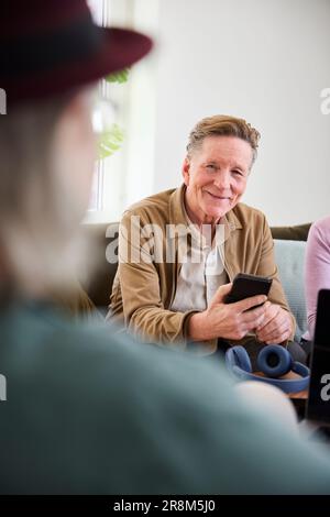 Smiling senior man in living room and holding cell phone Stock Photo