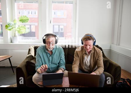 Senior men sitting in living room and using digital tablet and laptop to edit podcast Stock Photo