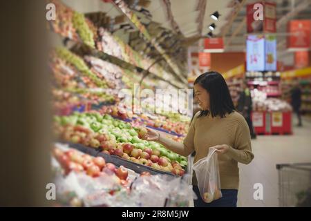 View of woman standing in supermarkets and putting apples into plastic bag Stock Photo
