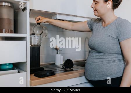 Pregnant woman preparing coffee in kitchen Stock Photo