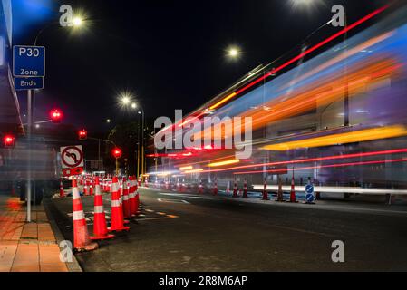 Orange traffic cones lined up on the road. Bus light trails approaching red traffic lights. Auckland. Stock Photo