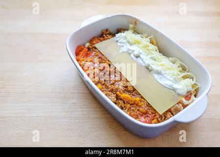 Cooking lasagna, layers of Bolognese sauce, flat pasta sheets, cream or bechamel and cheese in a casserole dish on a wooden kitchen table, copy space, Stock Photo