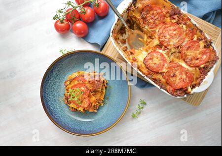 Lasagna, casserole dish of flat pasta sheets, ground beef, vegetables and tomatoes topped with melted cheese in a casserole and on a blue plate, high Stock Photo