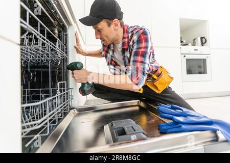 Worker using screwdriver to repair dishwasher at home stock photo Stock Photo