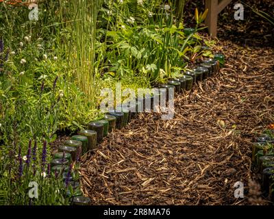 Bark chipping garden path edged with recycled wine bottles in a UK garden. Stock Photo