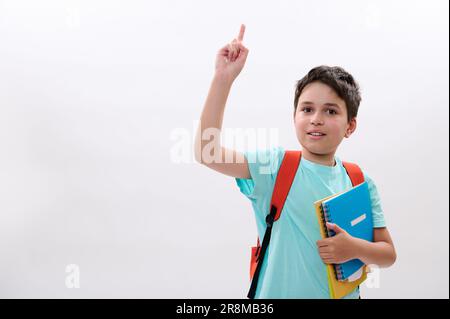 Smart schoolboy, handsome preteen boy smiles looking at camera, pointing aside a copy space on white isolated backdrop Stock Photo