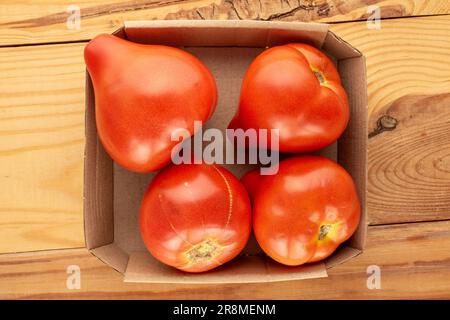 Several red tomatoes with paper tray on wooden table, macro, top view. Stock Photo