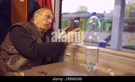 Elderly man traveling by train and taking pictures of the landscape through the window using a smartphone Stock Photo
