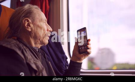 Elderly man traveling by train and taking pictures of the landscape through the window using a smartphone Stock Photo