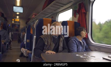 Elderly couple is riding in a train carriage and looking out the window Stock Photo