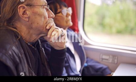 Elderly couple is riding in a train carriage and looking out the window Stock Photo