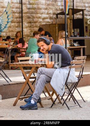 Young man at cafe table listening to music on headset - Tours, Indre-et-Loire (37), France. Stock Photo