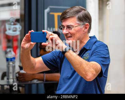 Smiling man in blue shirt and glasses holding mobile phone taking photo - Tours, Indre-et-Loire (37), France. Stock Photo