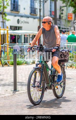 Man in T-shirt and shorts riding electric bike through city center - Tours, Indre-et-Loire (37), France. Stock Photo