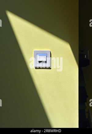 Electric Light Switch in sunlight on yellow wall with shadow. Stock Photo