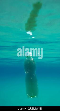 Green plastic bottle drifting under surface of blue water. Plastic pollution of Ocean, Discarded plastic bottle floats underwater in sunlight, Red Stock Photo