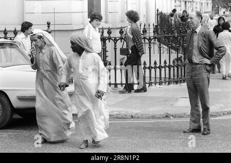 Poor Arabs in London with English Minder Harley Street watching whats going on. Middle Eastern people came to Britain for subsidised healthcare in Harley Street clinics. Two Arab men holding hands in Harley Street, while English chauffeur - minder watches and waits for his clients to exit their clinic. They mainly stayed in cheap hotels in Earls Court. London, England 1977 1970s UK HOMER SYKES Stock Photo