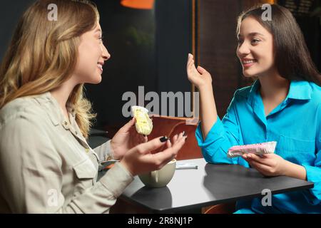 Young women with coffee and eclairs spending time together in cafe Stock Photo