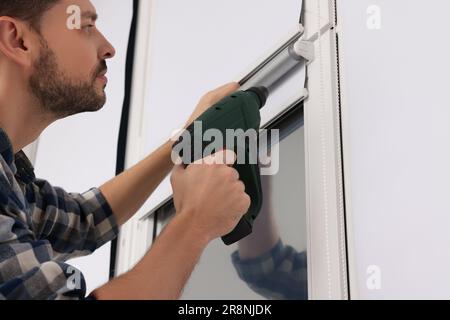 Man with drill installing roller window blind indoors, closeup Stock Photo