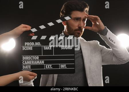 Actor performing while second assistant camera holding clapperboard on black background, closeup Stock Photo