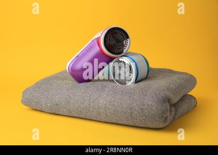 Modern fabric shavers and woolen clothes on yellow background Stock Photo