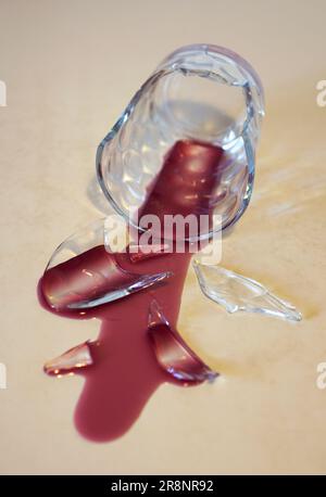 a broken glass lying on table with poured red wine Stock Photo