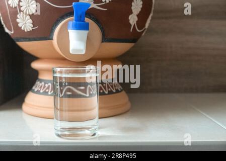 A glass of water from traditional water dispenser called Labu Sayong ...