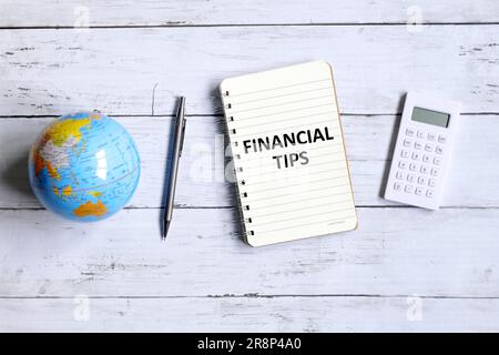 Top view of globe of world map,calculator,pen and notebook written with 'FINANCIAL TIPS' on white wooden background. Stock Photo