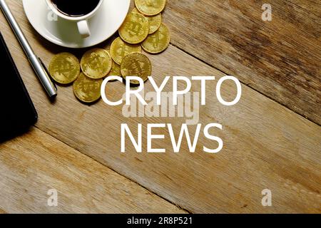 Top view of a cup of coffee,golden bitcoin replica,notebook and pen on wooden background written with CRYPTO NEWS. Stock Photo